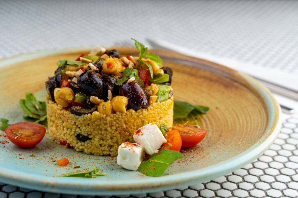 Délicieuse salade de couscous avec des olives, des pois chiches et des tomates cerises sur une assiette moderne.