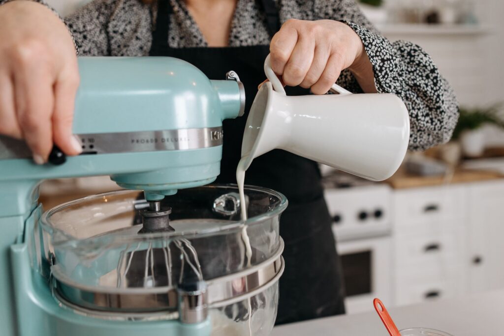 Personne dans une cuisine versant du lait dans un bol de batteur sur socle pendant la préparation de la pâtisserie.