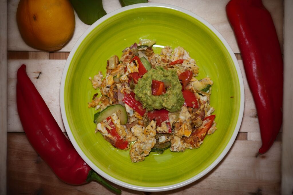 Plat vibrant à base d'œufs et de légumes, garni de guacamole et entouré de poivrons frais.