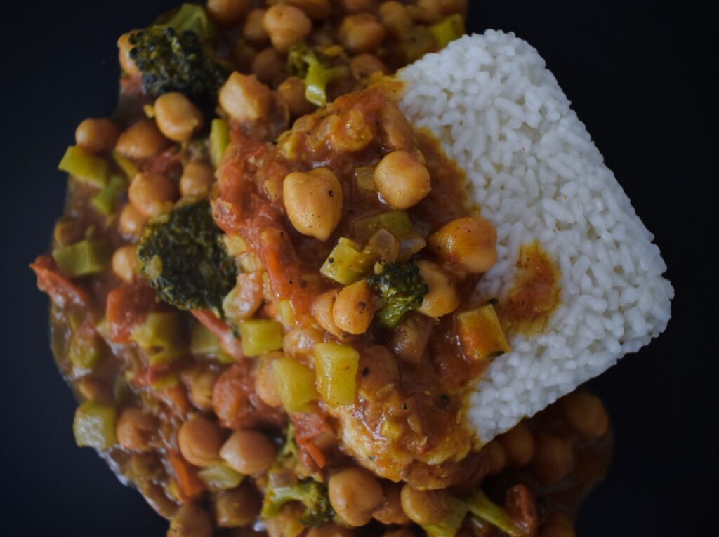 Délicieux ragoût de pois chiches végétalien avec du riz, photographié de dessus sur un fond noir.