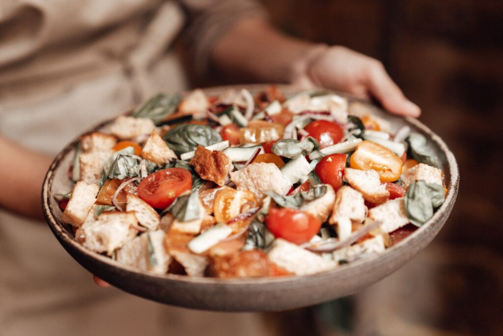 Délicieuse salade Panzanella servie sur un plat marron avec des légumes frais et des herbes.
