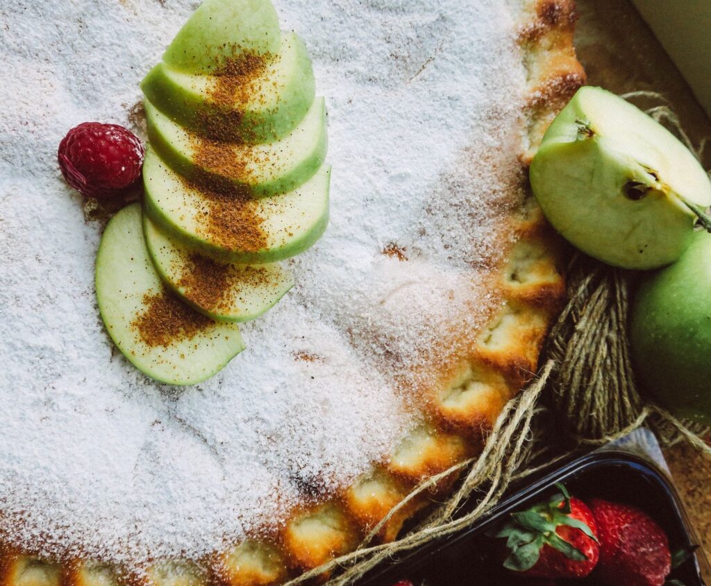 Vue de dessus d'une tarte aux pommes maison saupoudrée de sucre et entourée de fruits frais, parfaite pour les amateurs de desserts.