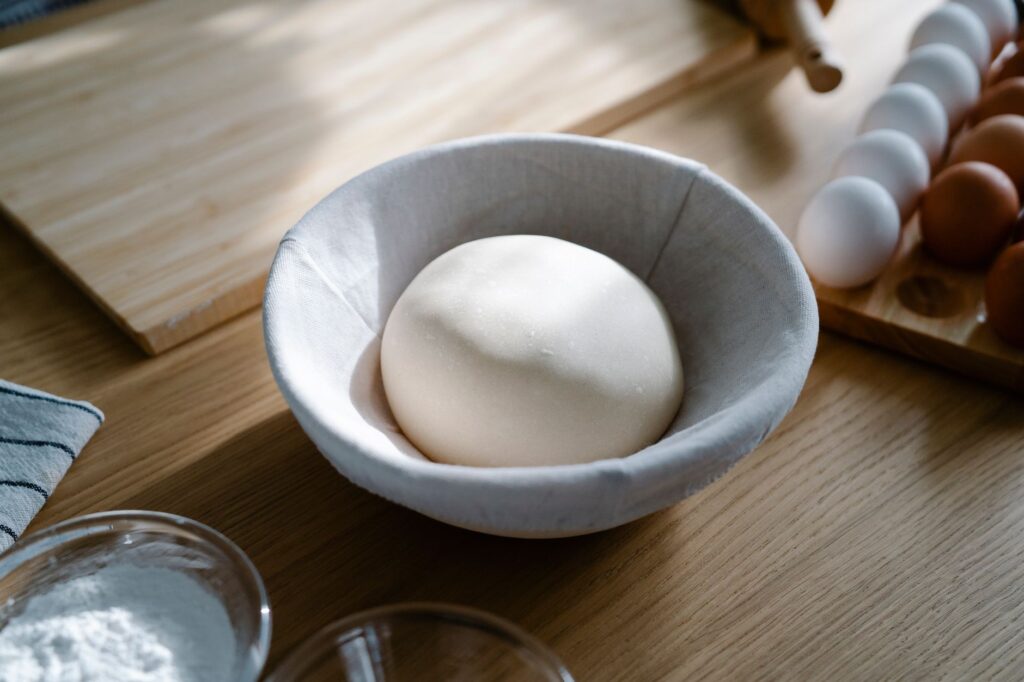 Pâte fraîche reposant dans un bol avec des œufs et de la farine sur un plan de travail en bois, idéale pour les scènes de pâtisserie.
