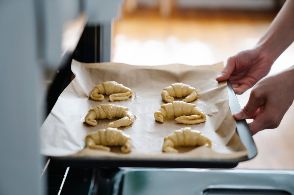 Des mains plaçant des croissants faits maison sur un plateau dans un four, prêts à cuire.