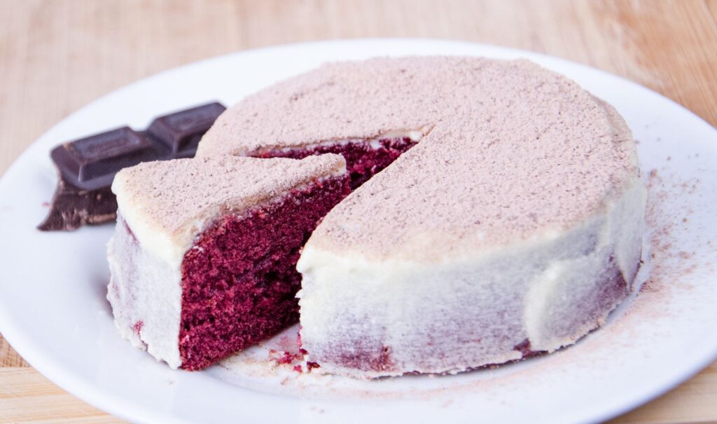 Gâteau rouge velours tranché avec glaçage au fromage à la crème sur une assiette blanche, parfait pour les amoureux des desserts.