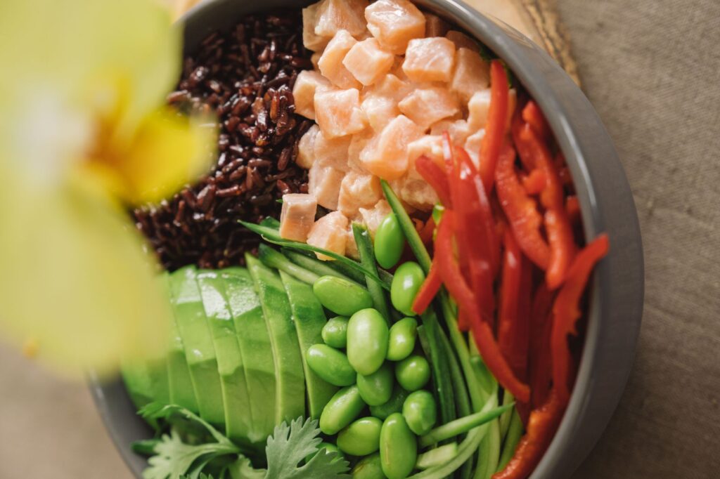Gros plan d'un bol de poke au saumon coloré avec avocat, poivrons rouges et riz noir.