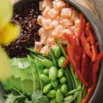 Gros plan d'un bol de poke au saumon coloré avec avocat, poivrons rouges et riz noir.