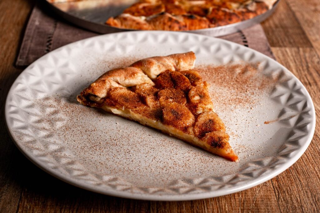 Gros plan d'une tranche de pizza dessert à la pomme et à la cannelle sur une assiette blanche.