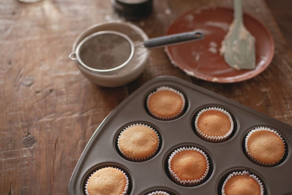 Des cupcakes tièdes sortent du four, disposés dans un moule à muffins sur une table rustique.