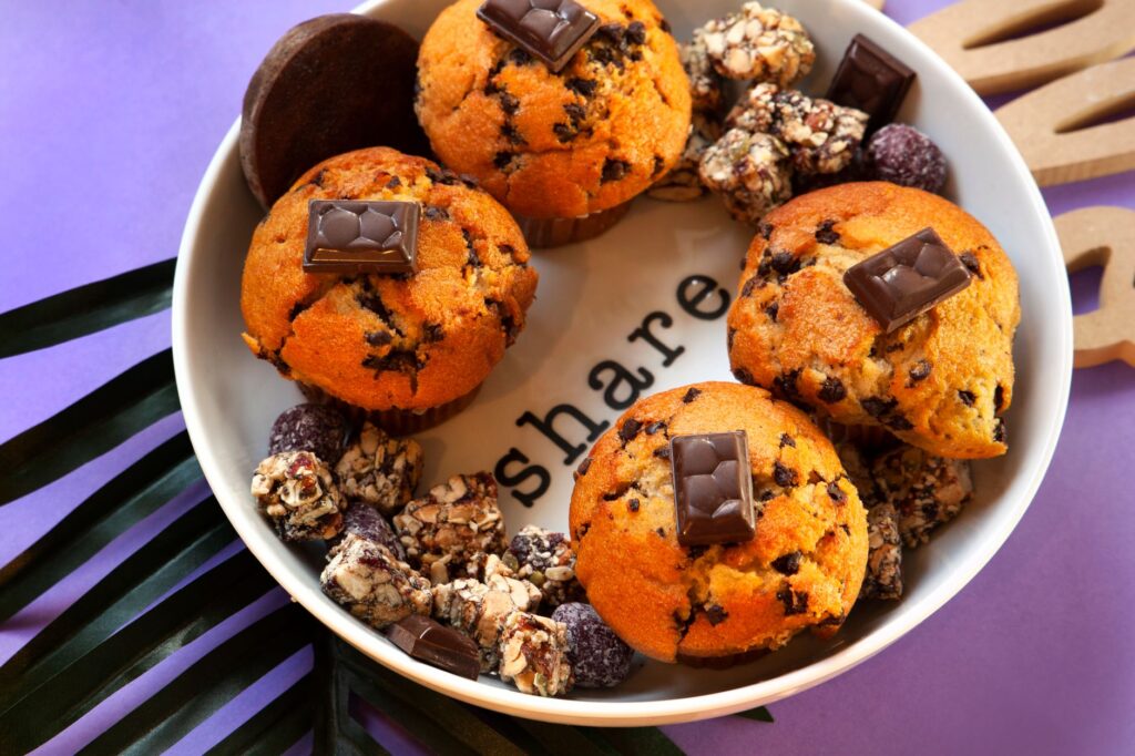 Savourez des muffins aux pépites de chocolat fraîchement cuits avec des friandises variées sur une assiette décorative.