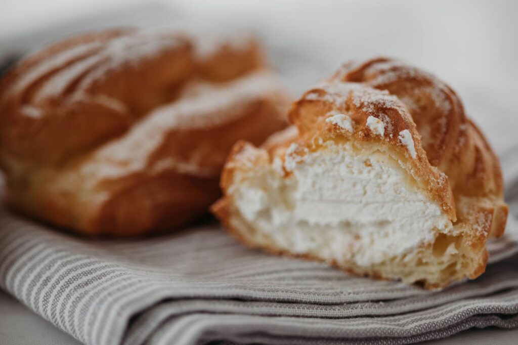 Gros plan sur un délicieux éclair fourré à la crème, saupoudré de sucre glace sur un tissu rayé.