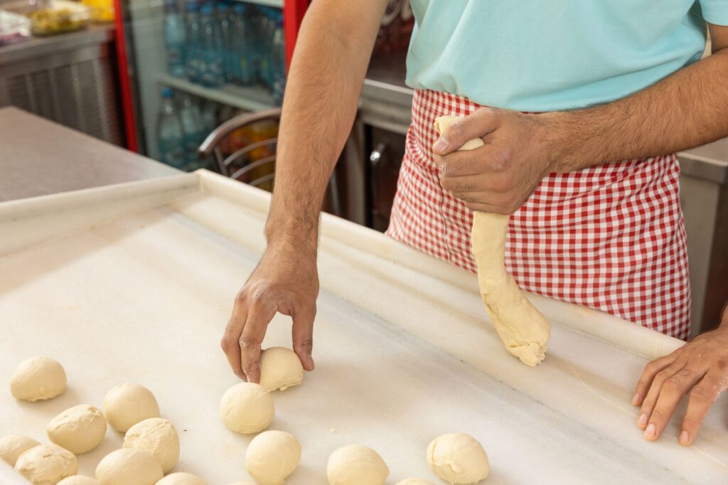 Homme pétrissant et façonnant la pâte sur un plan de travail blanc dans une cuisine professionnelle.