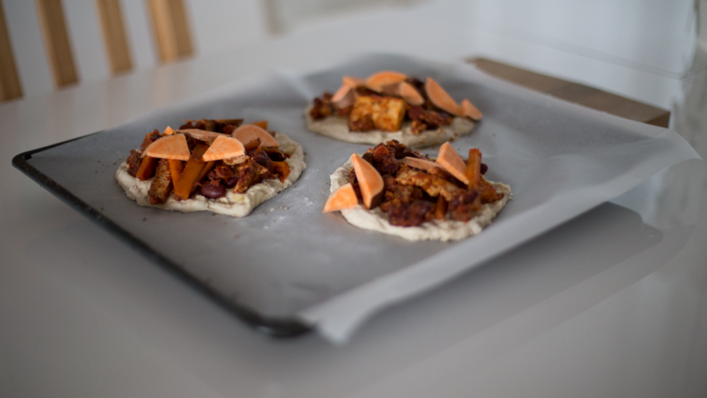 Mini pizzas fraîchement préparées avec des garnitures sur une plaque de cuisson, prêtes à enfourner.