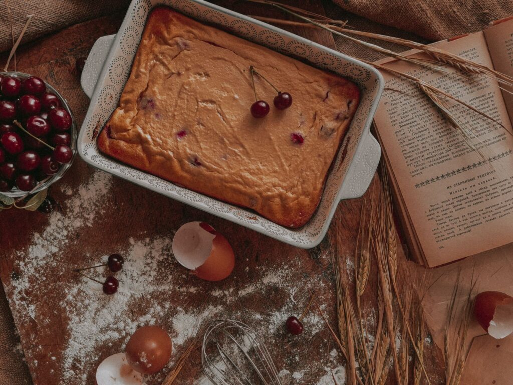 Délicieux gâteau aux cerises dans un cadre rustique avec des coquilles d'œufs, de la farine et un livre de cuisine ouvert pour l'inspiration de la pâtisserie.