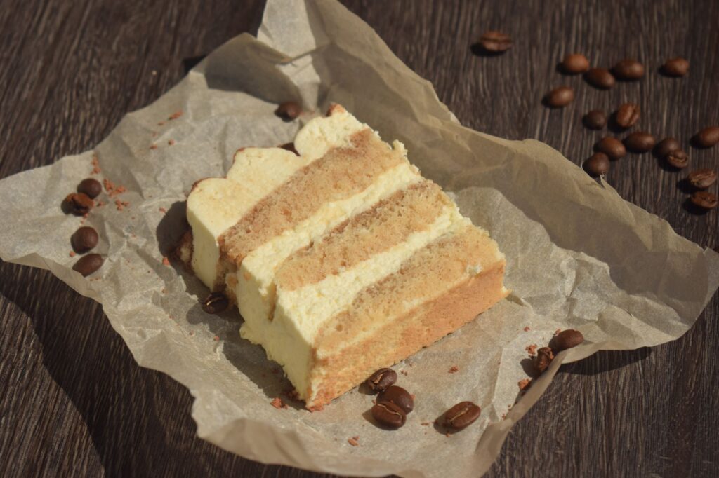 Une délicieuse part de gâteau tiramisu entourée de grains de café sur du papier sulfurisé.