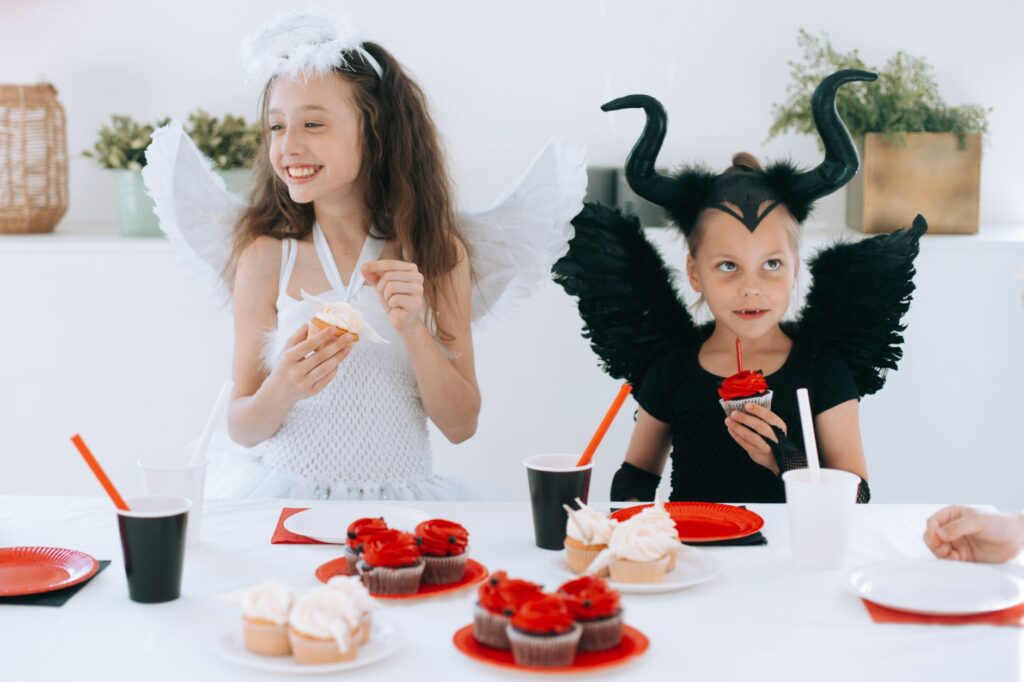 Des enfants déguisés en ange et en diable profitent de cupcakes lors d'une fête d'Halloween.
