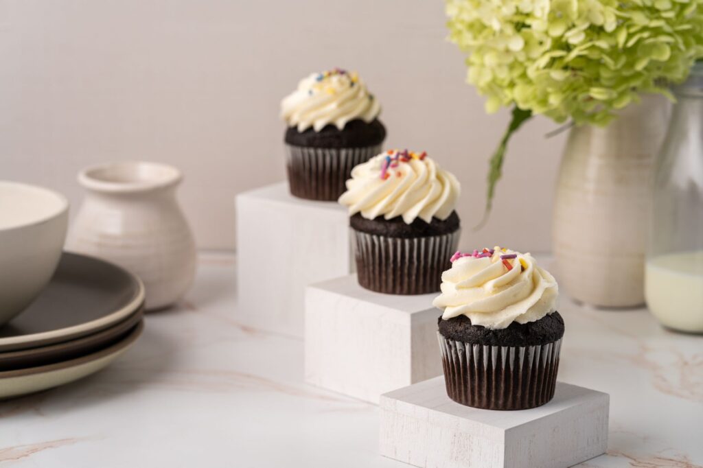 Trois cupcakes au chocolat avec un glaçage crémeux et des vermicelles, présentés élégamment avec des décorations.