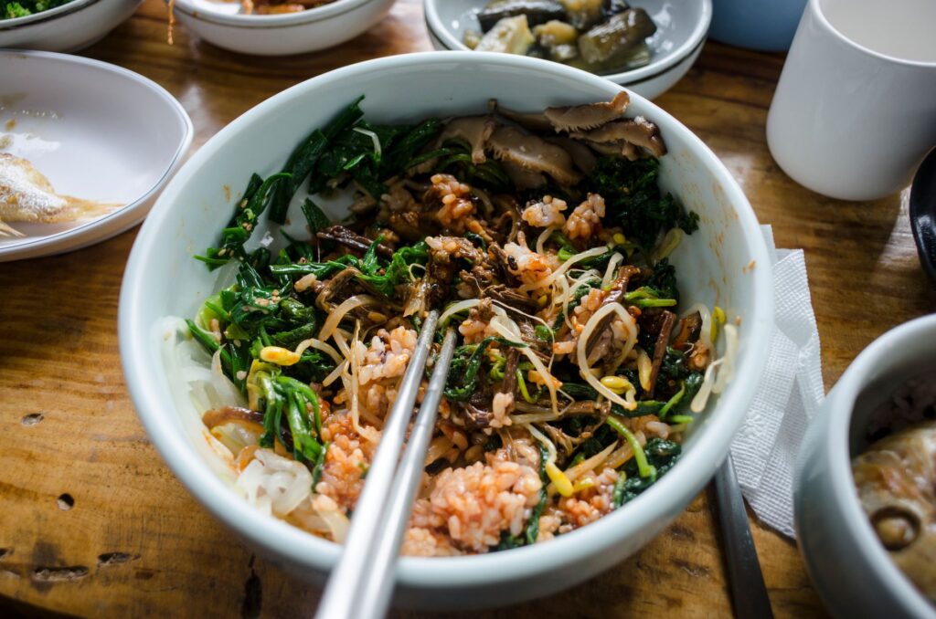 Un bol coloré de bibimbap coréen rempli de légumes mélangés, de riz et de champignons en gros plan.
