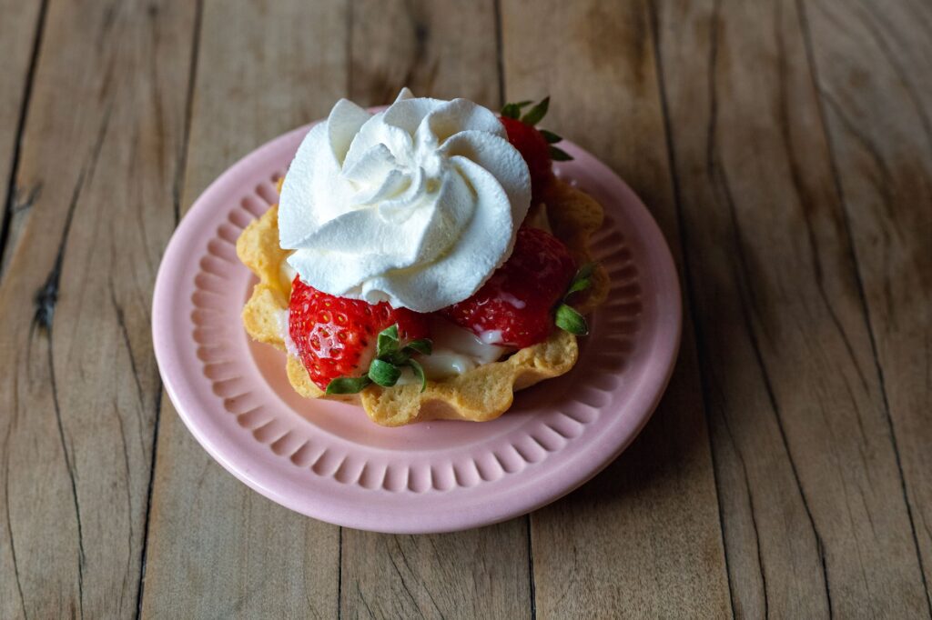 Délicieuse tarte aux fraises surmontée de crème fouettée, servie dans une assiette rose. Parfaite pour les amateurs de dessert.
