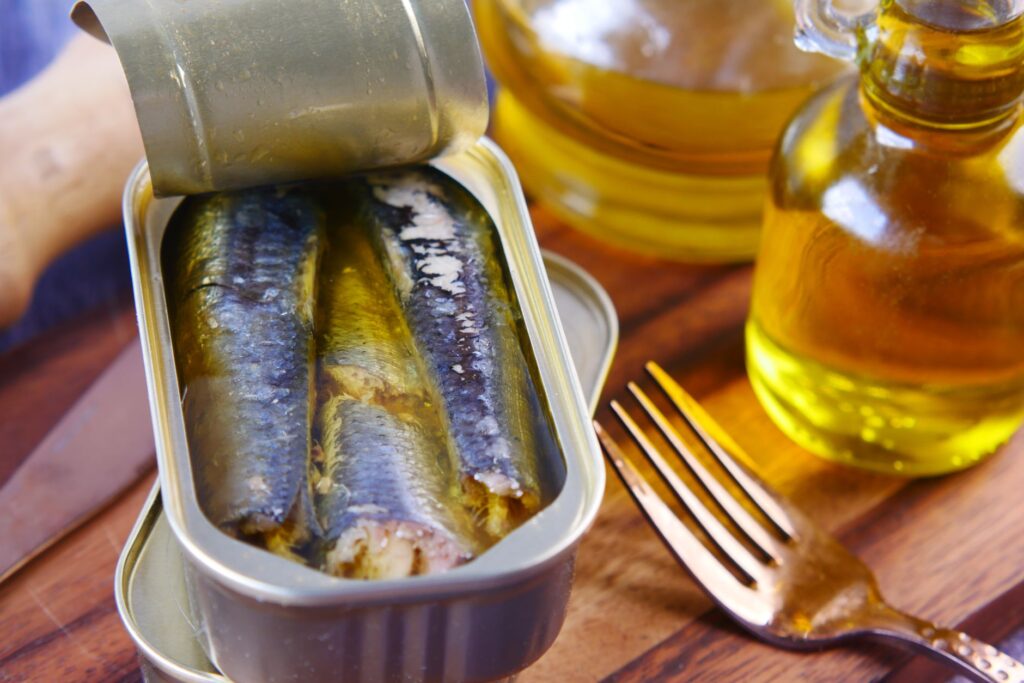 Gros plan de sardines en conserve dans de l'huile d'olive avec une fourchette sur une surface en bois.