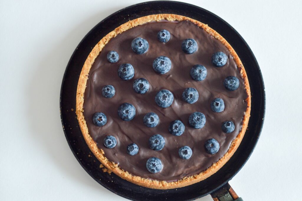 Vue de dessus d'une riche tarte au chocolat adornée de myrtilles fraîches sur une croûte rustique.