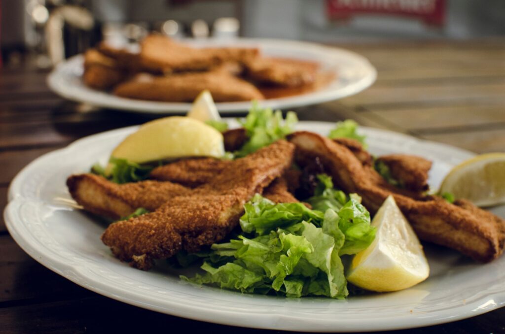 Poulet frit savoureux servi avec des quartiers de citron et de la laitue fraîche sur une assiette blanche.