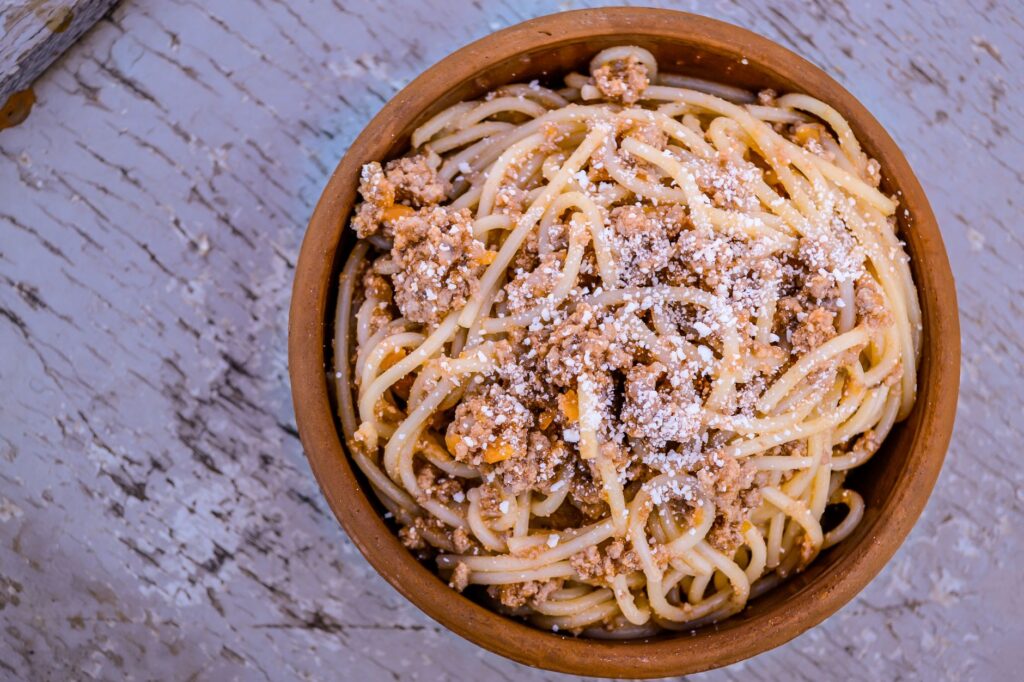 Gros plan d'un spaghetti bolognaise traditionnel servi dans un bol en bois rustique, garni de parmesan.